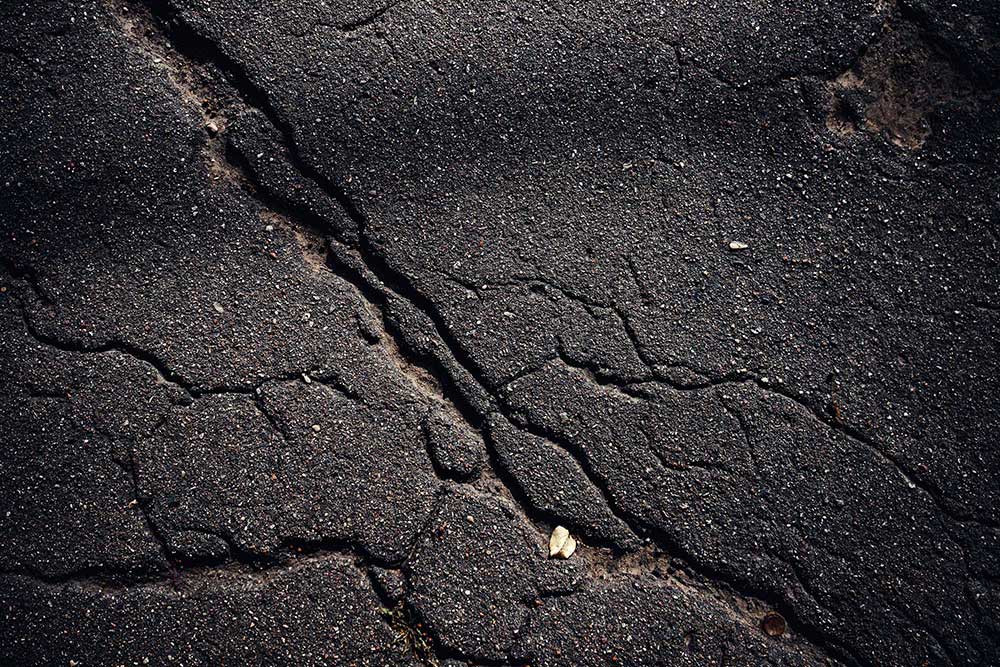 Cracked asphalt surface in need of sealcoating for protection.